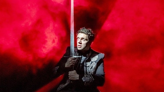 Schauspieler Christian Friedel, ein Mann in Ritterrüstung mit einem hoch aufgerichteten Schwert.