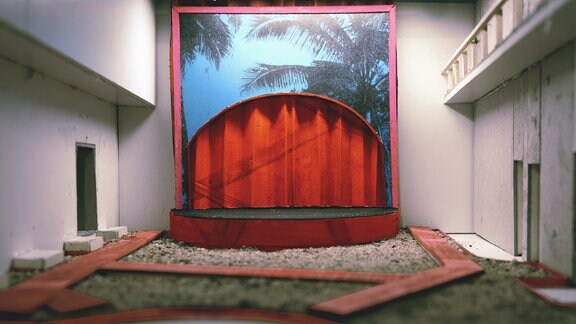 Ein Modell von einem Bühnenbild mit Palmenmotiv und rotem Theatervorhang
