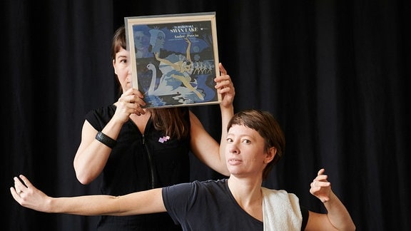 Zwei Frauen vor schwarzem Hintergrund - eine hält sich eine altes Cover einer Schallplatte von "Schwanensee" vor das Gesicht