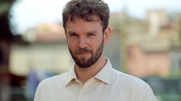 Timm Kröger, ein junger Mann mit weißem Hemd, Bart und dunklen Haaren. 