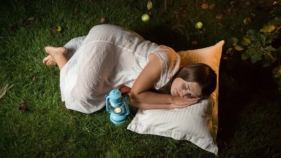 Eine Frau liegt im Freien auf Kissen und träumt.