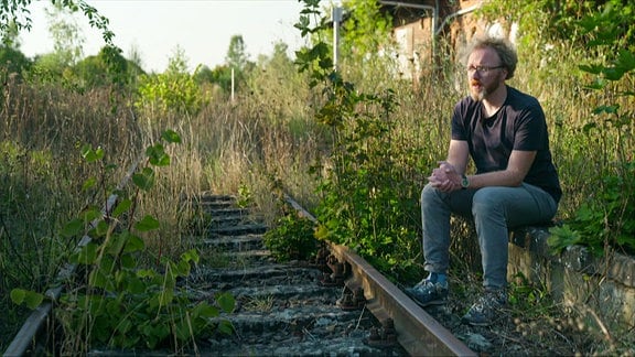 Ein Mann sitzt neben einem verwaisten Bahngleis