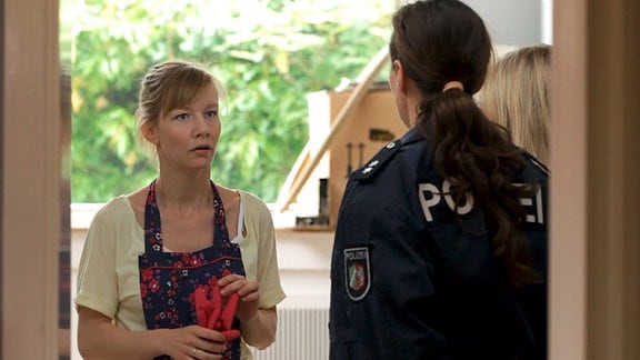 Schauspielerin Sandra Hüller in einer Szene des Films "Über uns das All", sie trägt eine Schürze, vor ihr steht eine Polizistin.
