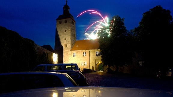Ein Feuerwerk über der Wasserburg in Egeln, einem angestrahlten Gebäuse mit Turm in sonst dunkler Umgebung.