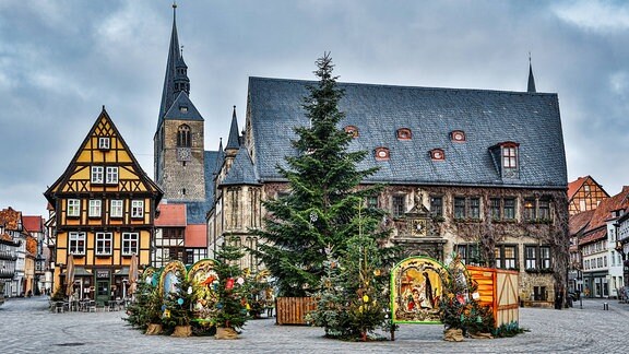 Ein großer Weihnachtsbaum und einige Buden auf einem Marktplatz vor einer Kirche und einem Fachwerkhaus.