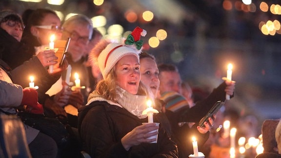 Menschen mit Kerzen in der Hand nehmen an einem Weihnachtssingen teil