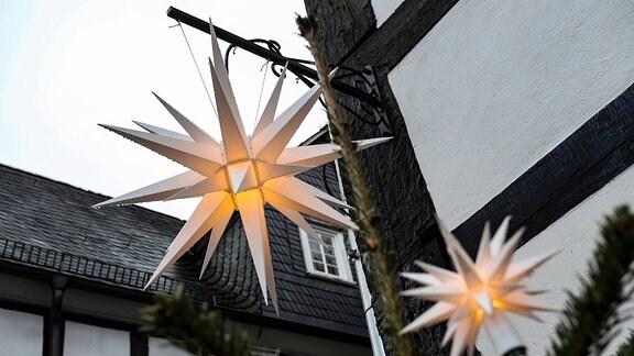 Zwei leuchtende Weihnachtssterne hängen an einem Fachwerkhaus.