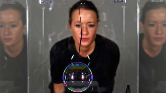 Eine Frau betrachtet eine Kunstinstallation, bei der eine Seifenblase in einem durchsichtigen Kasten schwebt. 