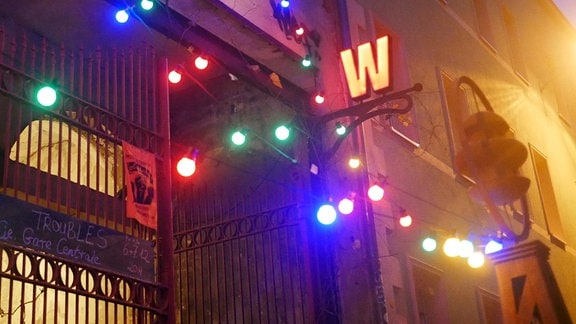 Fassade mit einem großen Tor, Lichterkette und einem leuchtenen W-Zeichen.