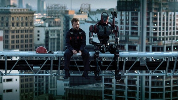 Mann und Roboter sitzen auf einem Stahlgerüst