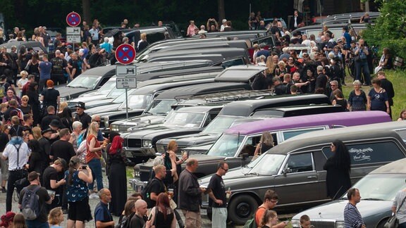 Besucherinnen und Besucher betrachten Oldtimer Leichenwagen während des Leichenwagen Treffens beim Wave-Gotik-Festival.