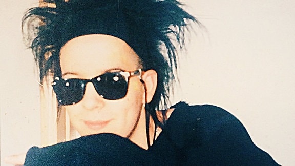 Ein junger Mann mit toupiertem schwarzen Haar und schwarzer Sonnenbrille