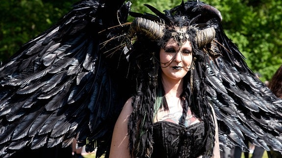Eine Besucherin des WGT in schwarzer Verkleidung mit Flügeln und Hörnern. 