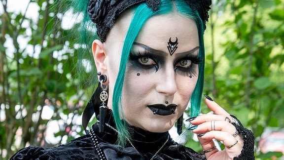 Eine Anhängerin der Gothic-Szene beim Wave-Gotik-Treffen 2022: Die Frau trägt dunkles Augen-Makeup, schwarzen Blumenkopfschmuck und hat grüne Haare.