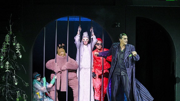 Wunschpunsch am Staatsschauspiel Dresden, mehrere Personen in Kostümen stehen auf einer Bühne hinter Gitterstäben