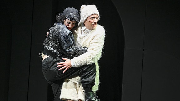 "Wunschpunsch" am Staatsschauspiel Dresden, eine Frau in einem schwarzen Kostüm umarmt eine Person in weißem Kostüm.