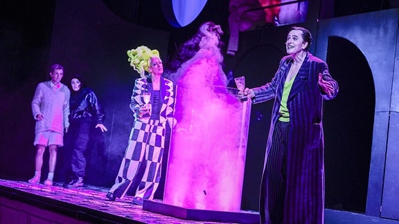 Szene aus dem Stück "Wunschpunsch", zwei Personen stehen neben einem Gefäß aus dem rosa Dampf steigt. 