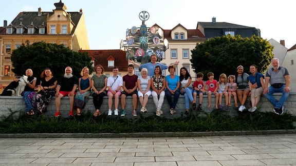 Mehrere Menschen sitzen in Reihe auf einer kleinen Mauer