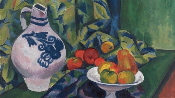 Zu sehen ist ein expressionistisches Gemälde von Max Pechstein: eine Obstschale steht auf einem Tisch, auf diesem ist auch ein Krug und ein Tuch