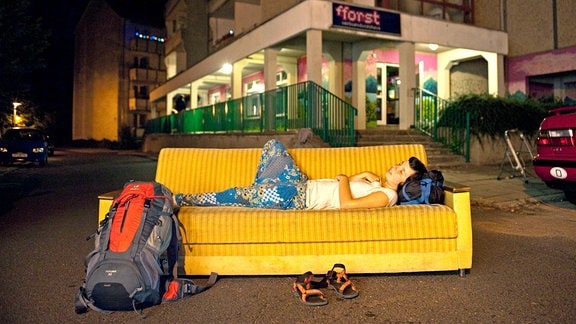 Eine COuchsurferin liegt mitten auf einer Straße auf einer Couch.