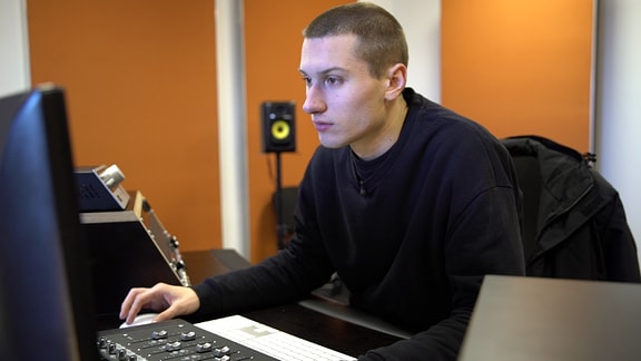 Ein junger Mann mit raspelkurzen Haaren blickt auf einen Computerbildschirm.