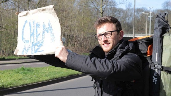 Road-Trip "4 Tage, 3 Länder - ohne einen Cent" - Dominik beim Trampen mit Schild "Chemnitz"