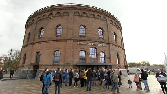 Planetarium Halle, einer runder Ziegelbau, davor stehen Menschen