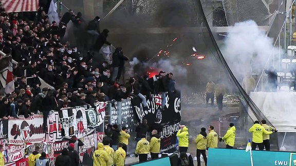 Während eines Fußballspiels schmeißen Fans unter den Augen von Security Feuerwerkskörper.