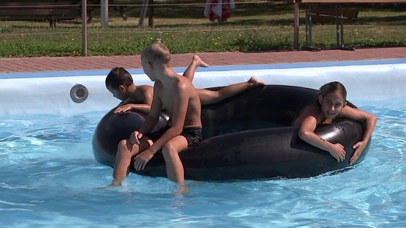 Drei Kinder sitzen auf einem großen Schwimmring.