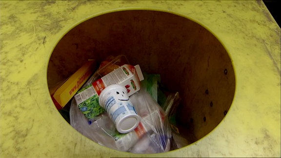 Auf einem Plastikbecher in einem Mülleimer ist ein Gesicht aufgemalt.