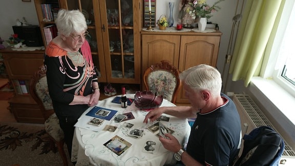 Eine Frau und ein Mann schauen sich Bilder auf einem Wohnzimmertisch an.