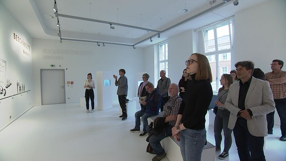 Besuchende stehen in einem weißen Museumsraum.
