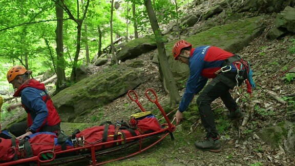 Zwei Personen der Bergwacht mit einer Trage im Wald.