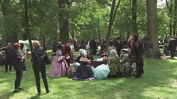 Verkleidete Menschen sitzen in einem Park.