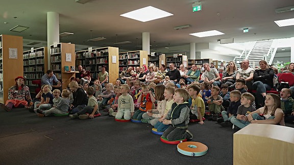 Kinder haben sich für eine Veranstaltung in einer Bibliothek auf dem Boden verteilt.