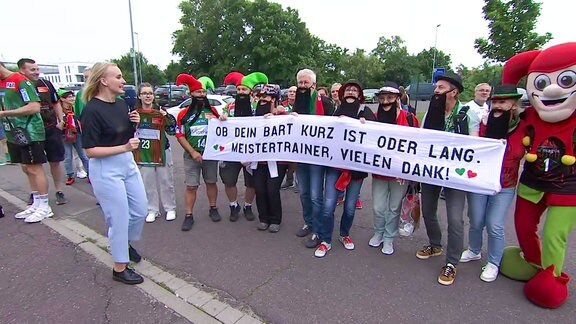 Eine Reporterin steht bei Fans, die ein Banner halten