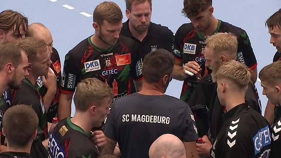 Die Handballmannschaft des SC Magdeburg steht versammelt um ihren Trainer.