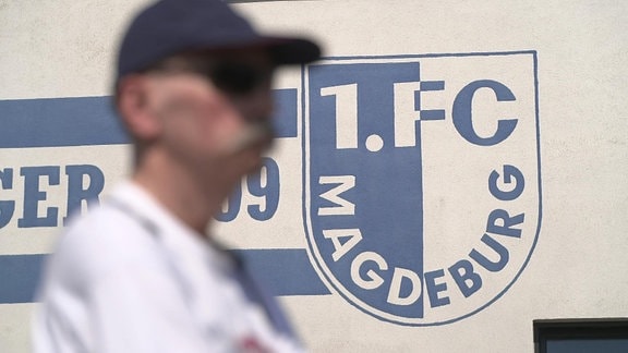 Fan steht vor einer Wand mit FC Magdeburg Logo