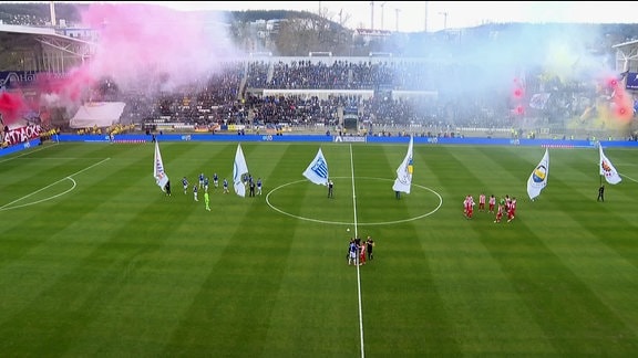 Menschen stehen mit großen Fahnen auf einem Fussballfeld.