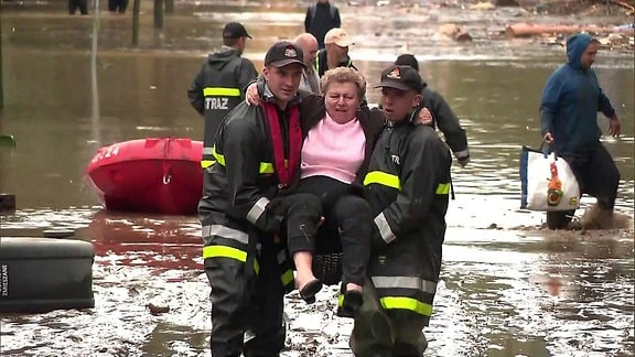 Zwei Hilfskräfte tragen eine ältere Frau durchs Hochwasser