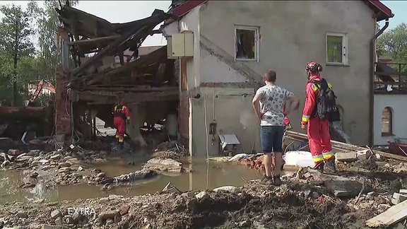 Menschen stehen vor den Trümmern eines duch die fluten zerstörten Wohnhauses