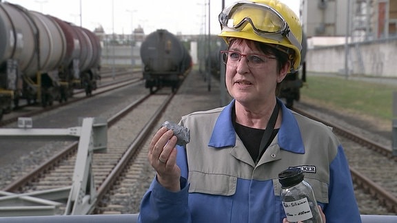 Eine Chemie-Mitarbeiterin erklärt ihr Produkt vor einer Gleisanlage mit Kesselwaggons.