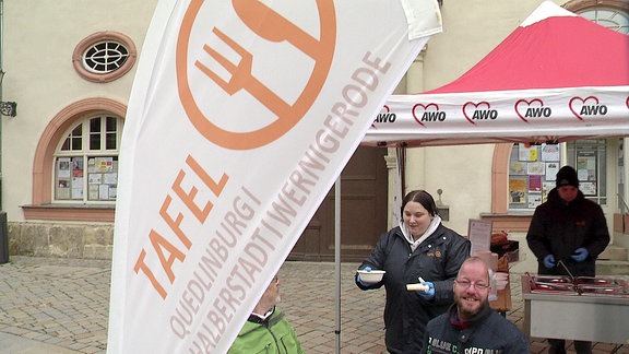 Eine Frau holt sich Essen im Vordergrund Fahne mit dem Logo der Tafeln