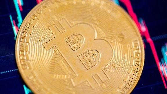 Eine Bitcoin-Münze liegt auf einem Bildschirm, der den Bitcoin - US-Dollar Kurs zeigt.