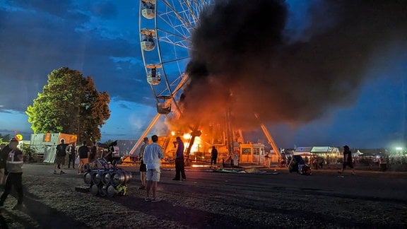 Besucher des Highfield-Festivals blicken auf ein Riesenrad, an dem Flammen zu sehen sind.