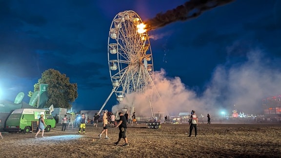 Besucher des Highfield-Festivals und Helfer blicken auf ein Riesenrad, an dem Flammen zu sehen sind.