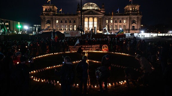 Menschen bauen auf einer Demonstration mit Kerzen im Gedenken an die Opfer des Krieges in der Ukraine vor dem Reichstagsgebäudes ein Peace-Zeichen. 