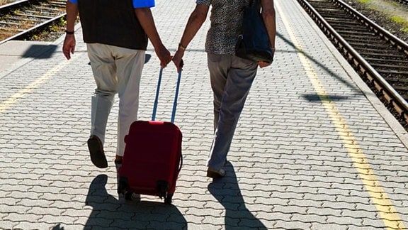 Zwei Personen mit Koffer auf einem Bahnsteig.
