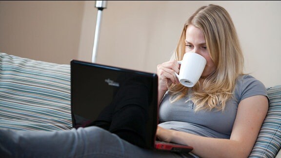 Eine kaffeetrinkende Frau schaut auf einen Laptop