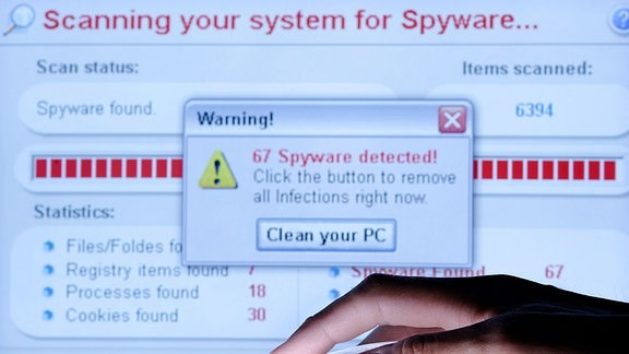 Eine Hand auf einer Maus vor einem Computermonitor, auf dem eine Virenwarnung angezeigt wird